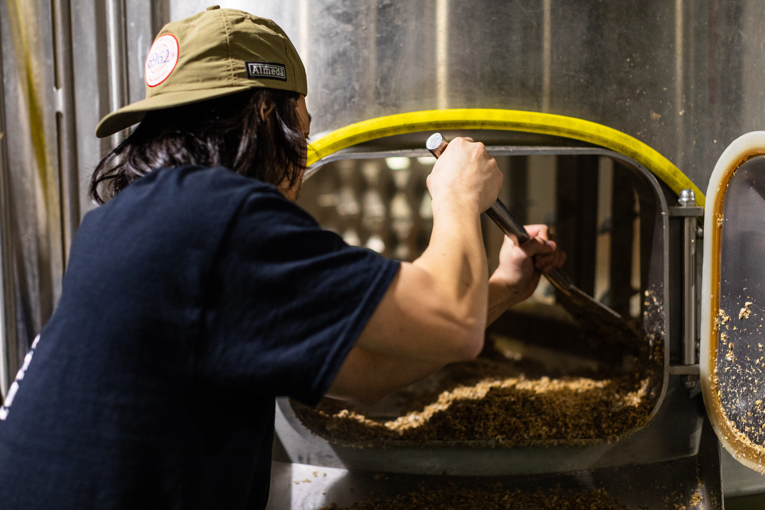 A brewer working with grain at the mash vessel